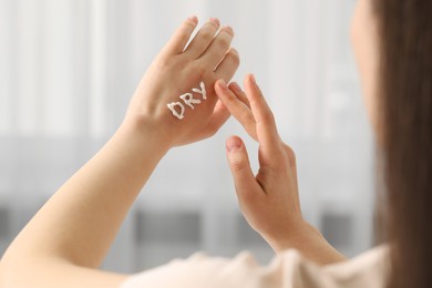 Photo of Young woman with word Dry made of cream on her hand indoors, closeup