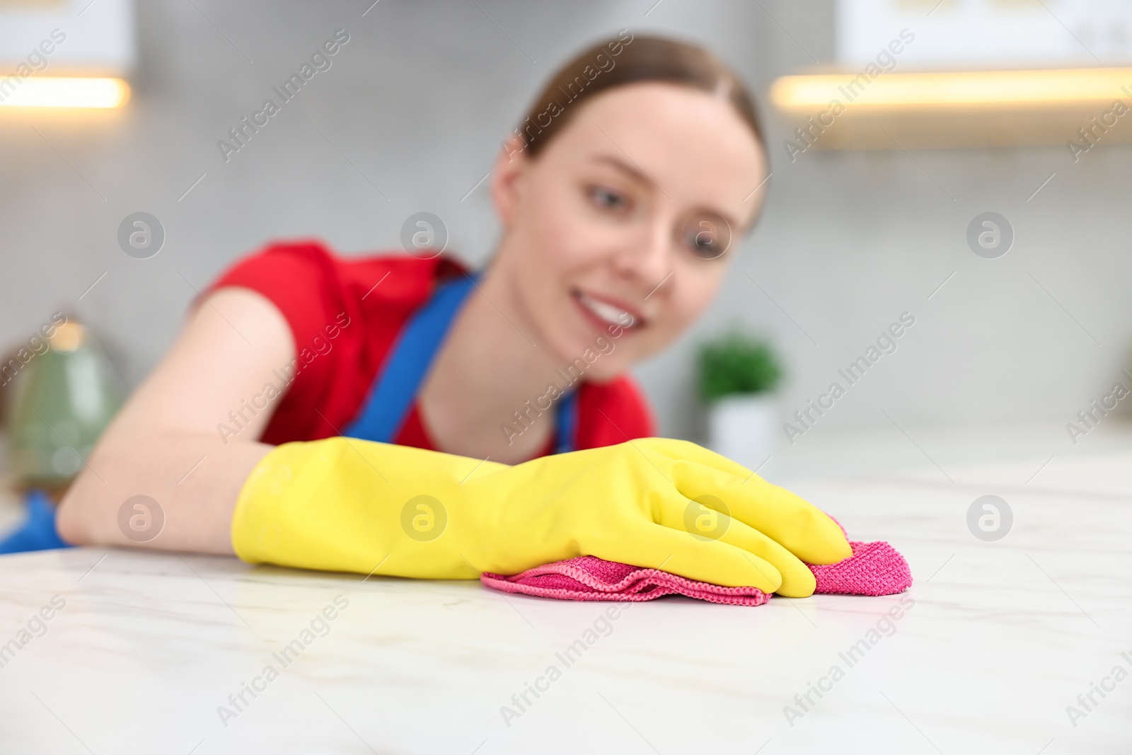 Photo of Woman cleaning white marble table with rag in kitchen, selective focus