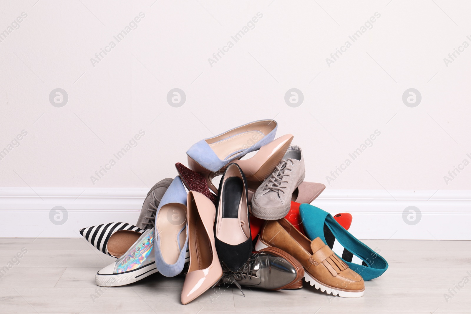 Photo of Heap of different shoes on floor against light wall