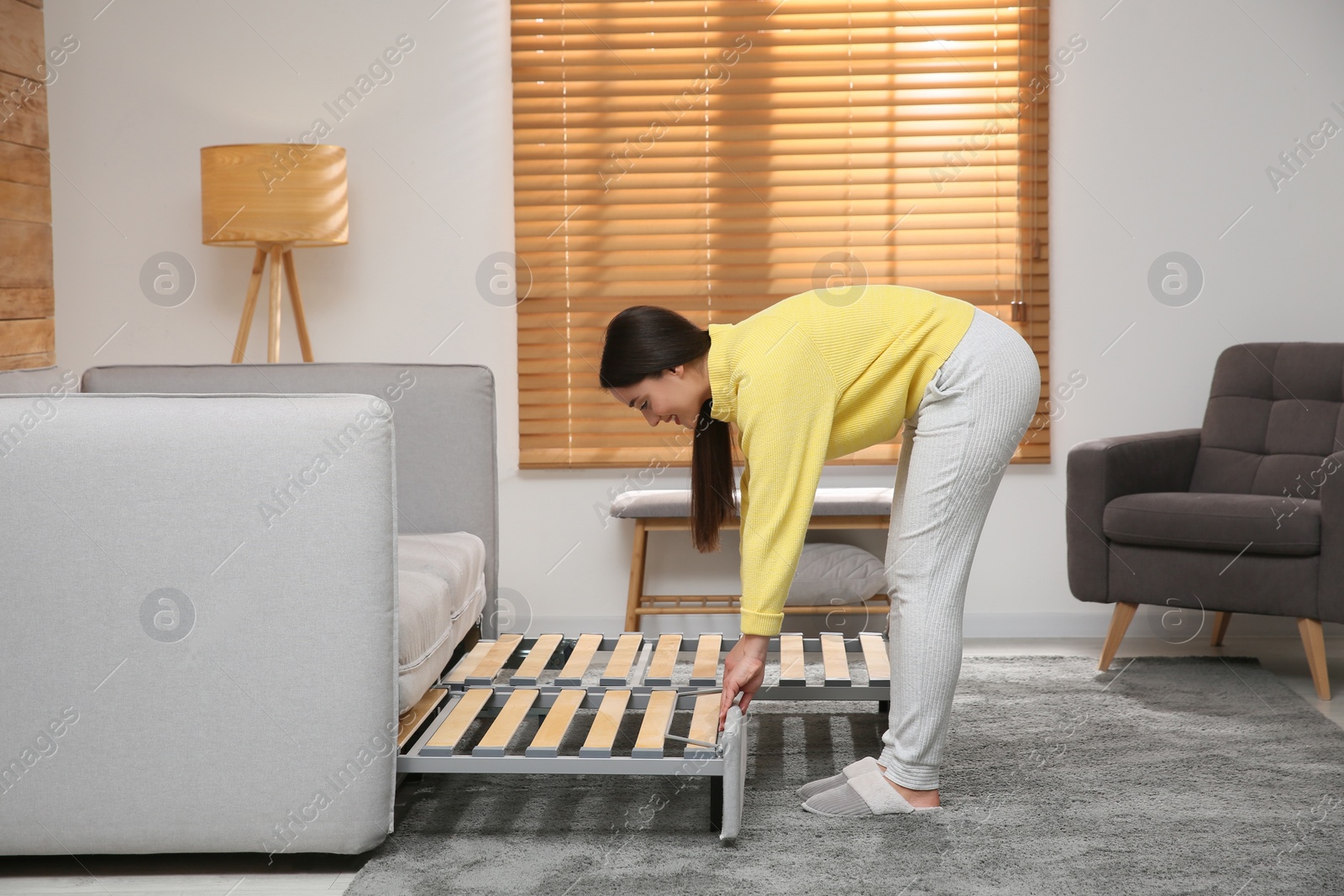 Photo of Young woman unfolding sofa into a bed in room. Modern interior