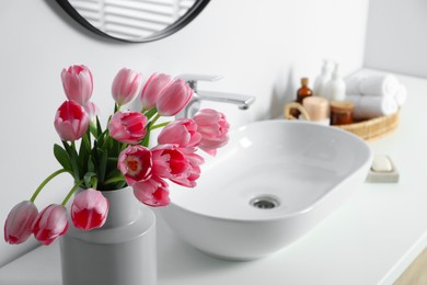 Vase with beautiful pink tulips and toiletries near sink in bathroom