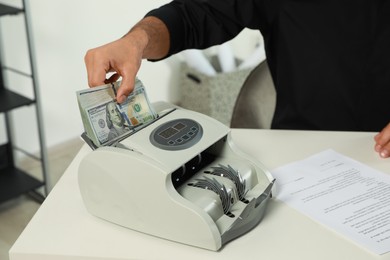 Photo of Man putting money into banknote counter at white table indoors, closeup