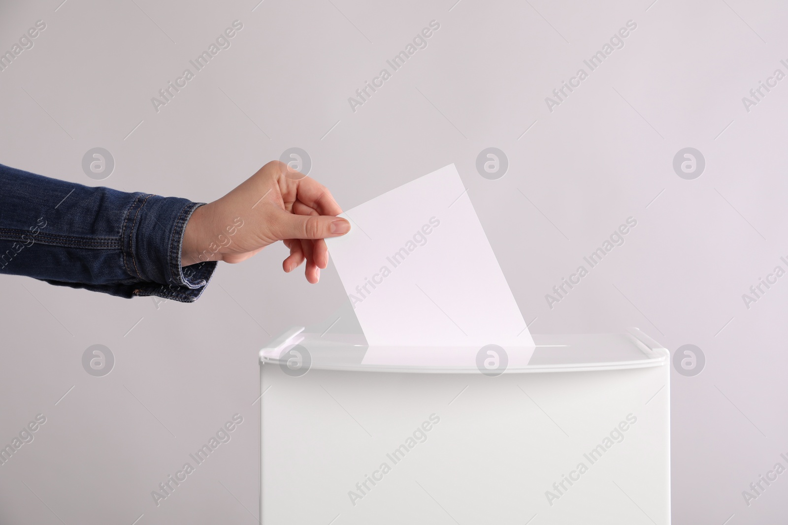 Photo of Woman putting her vote into ballot box on light grey background, closeup