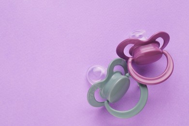 Photo of New baby pacifiers on purple background, flat lay. Space for text