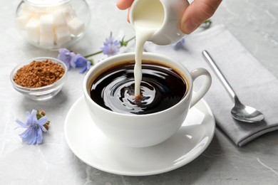 Photo of Woman pouring milk into cup with delicious chicory drink at light grey marble table, closeup