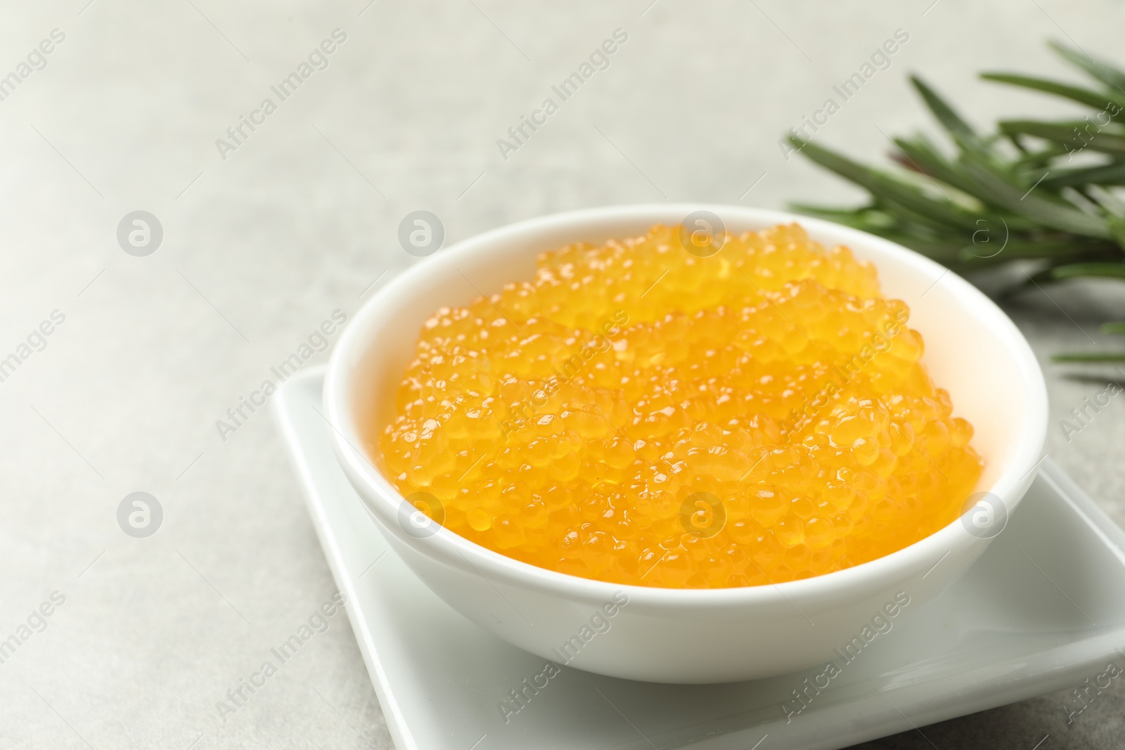 Photo of Fresh pike caviar in bowl and rosemary on light grey table, closeup