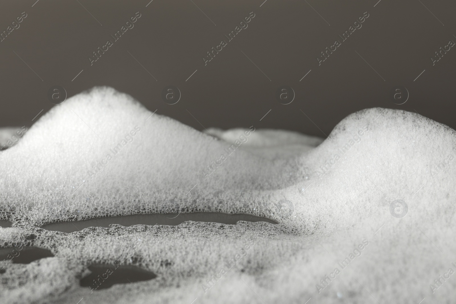 Photo of Fluffy bath foam on grey background, closeup