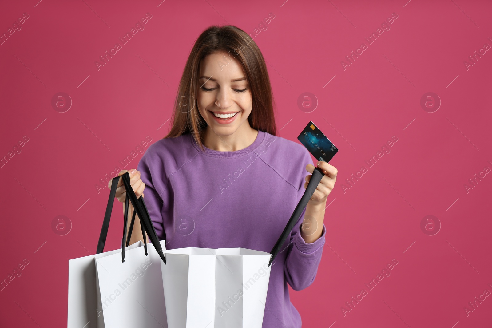 Photo of Happy young woman with credit card and shopping bags on pink background. Spending money