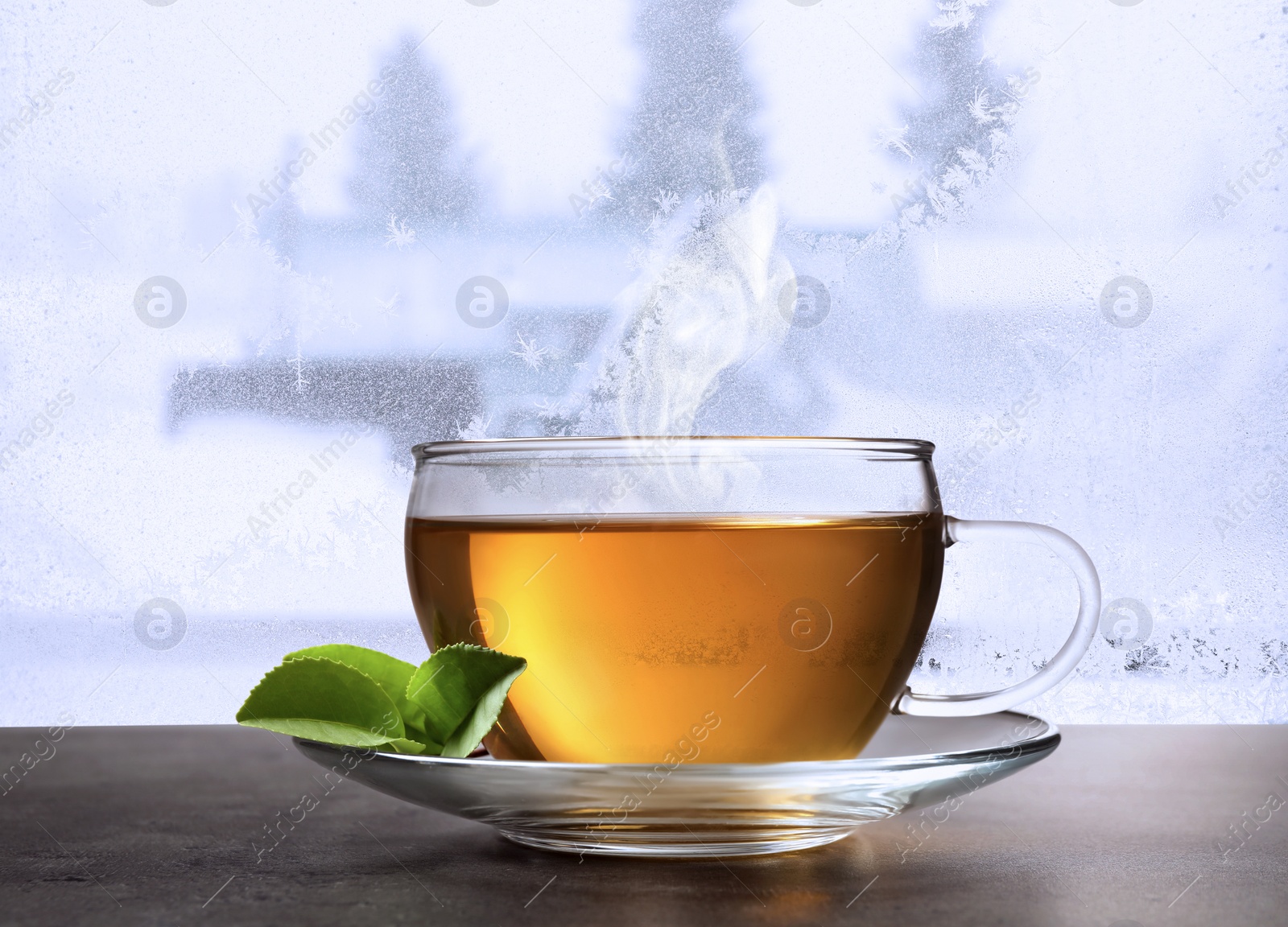 Image of Cup of hot tea on table near window covered with frost 