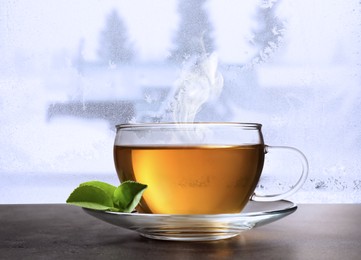 Image of Cup of hot tea on table near window covered with frost 