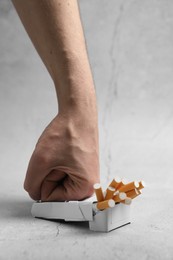 Stop smoking. Man crushing pack with cigarettes on light background, closeup