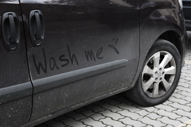 Inscription WASH ME and sad smiley on dirty car outdoors, closeup