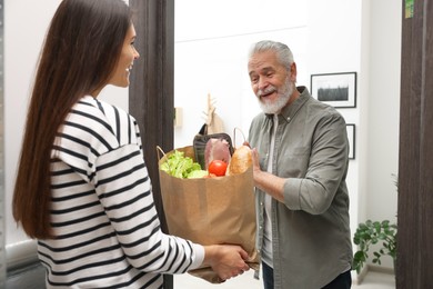 Courier giving paper bag with food products to senior man indoors