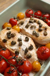 Photo of Delicious chicken fillets with capers, tomatoes and sauce in baking dish, closeup