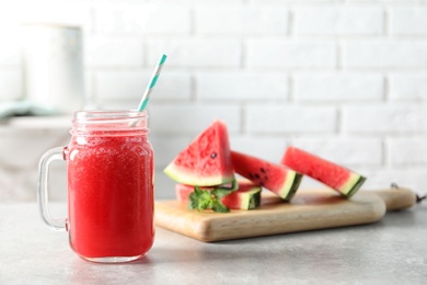 Photo of Tasty summer watermelon drink in mason jar and board with sliced fruit on table