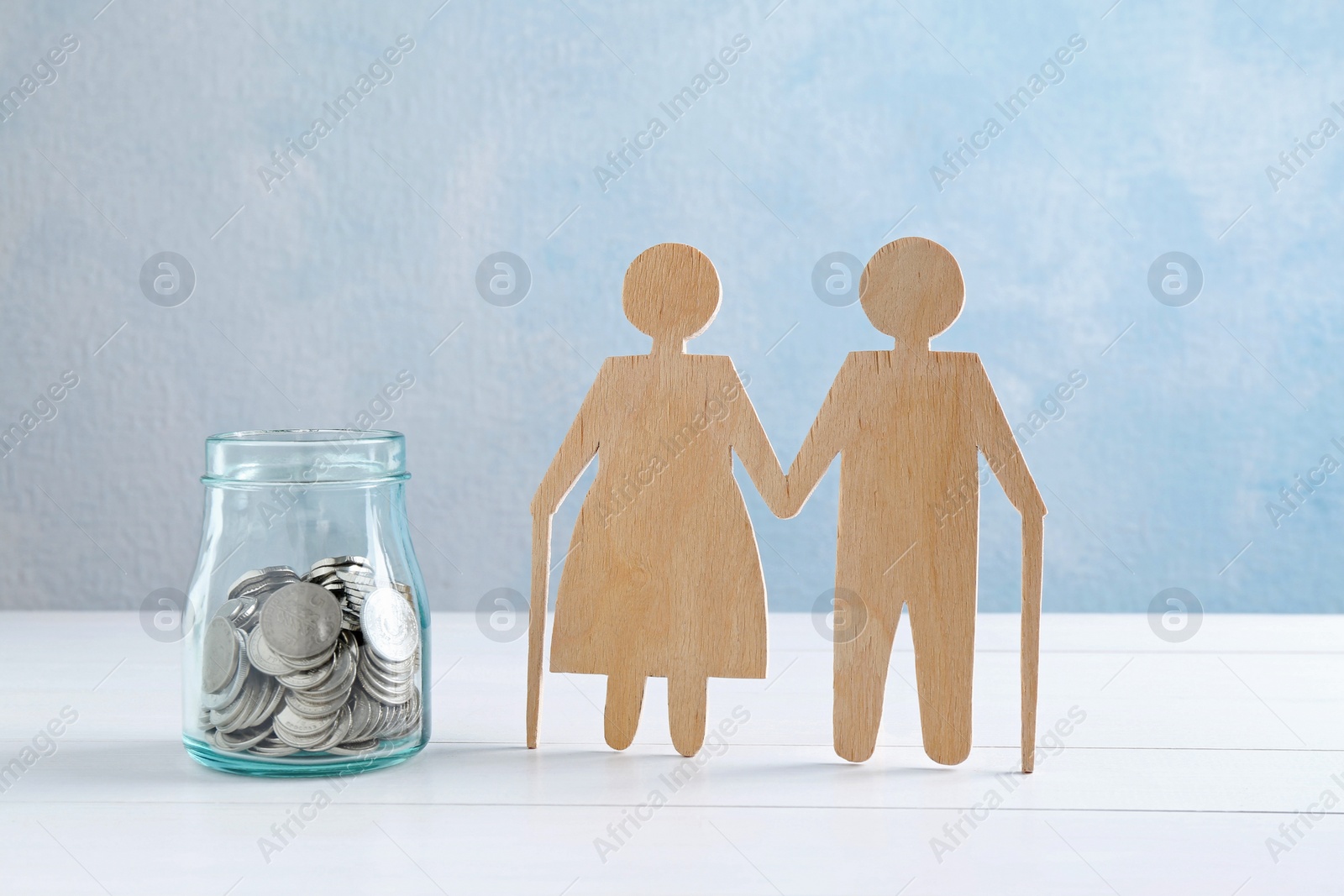 Photo of Pension savings. Figure of senior couple and jar of coins on white wooden table