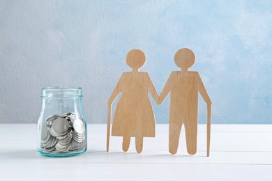 Pension savings. Figure of senior couple and jar of coins on white wooden table