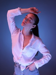 Portrait of beautiful young woman posing on blue background with neon lights