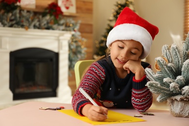 Photo of Cute child writing letter to Santa Claus at table indoors. Christmas tradition