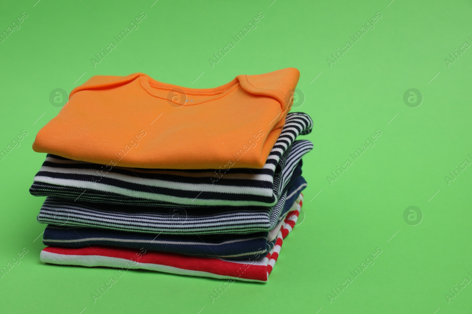 Photo of Stack of clean baby clothes on light green background. Space for text