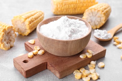 Photo of Bowl with corn starch and kernels on light grey table, closeup