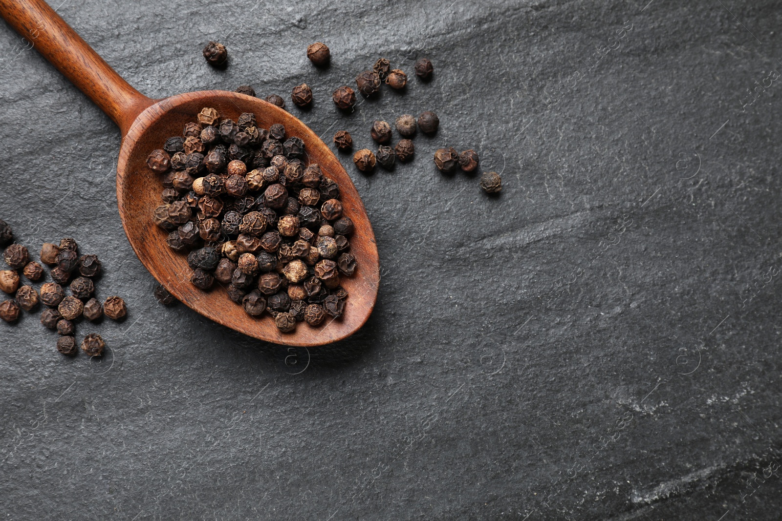 Photo of Aromatic spice. Pepper in spoon on black table, top view. Space for text