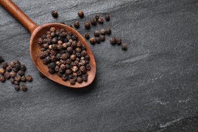 Aromatic spice. Pepper in spoon on black table, top view. Space for text