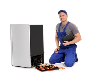 Male technician with clipboard and tools near broken refrigerator on white background