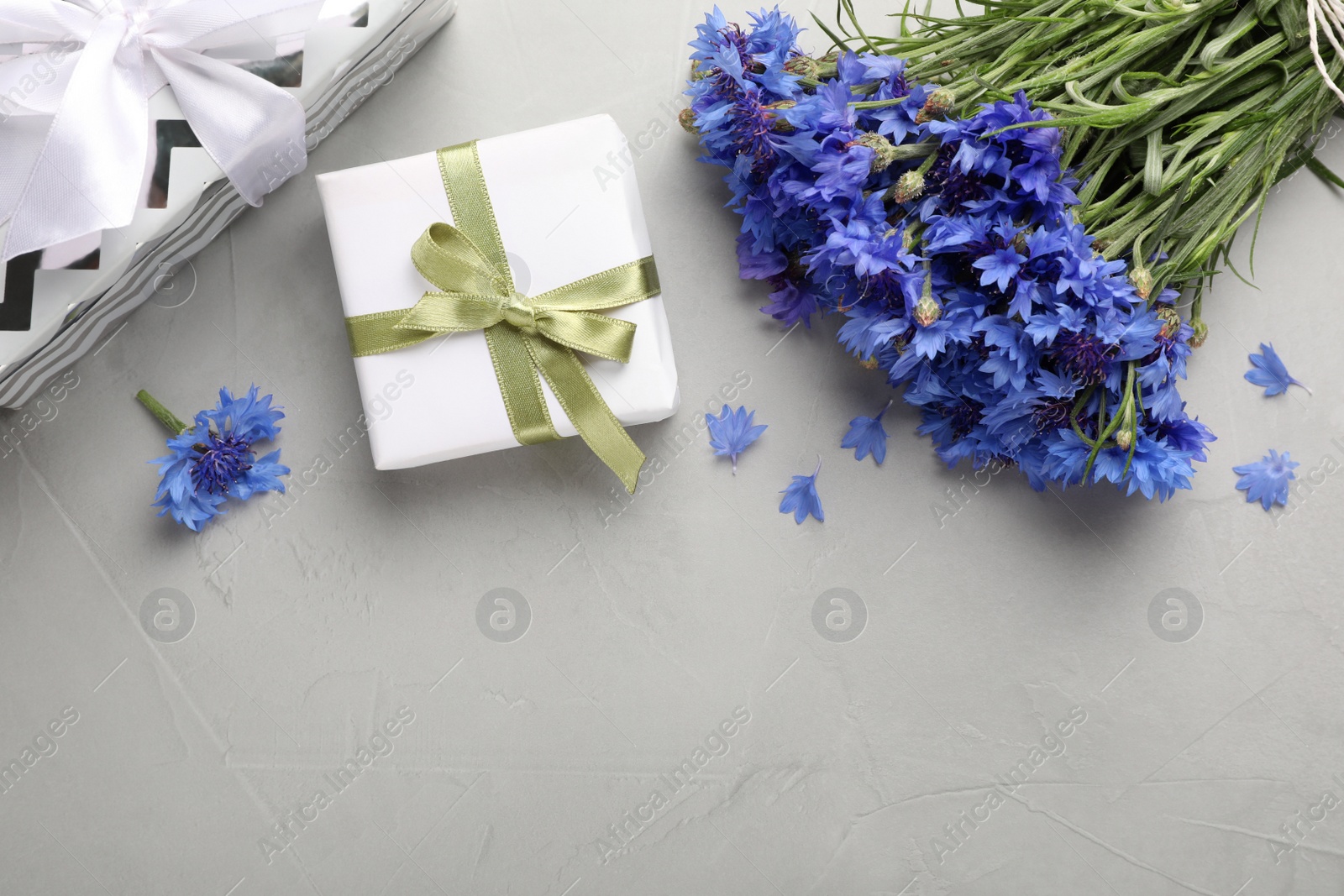 Photo of Bouquet of beautiful cornflowers and gift boxes on light table, flat lay. Space for text