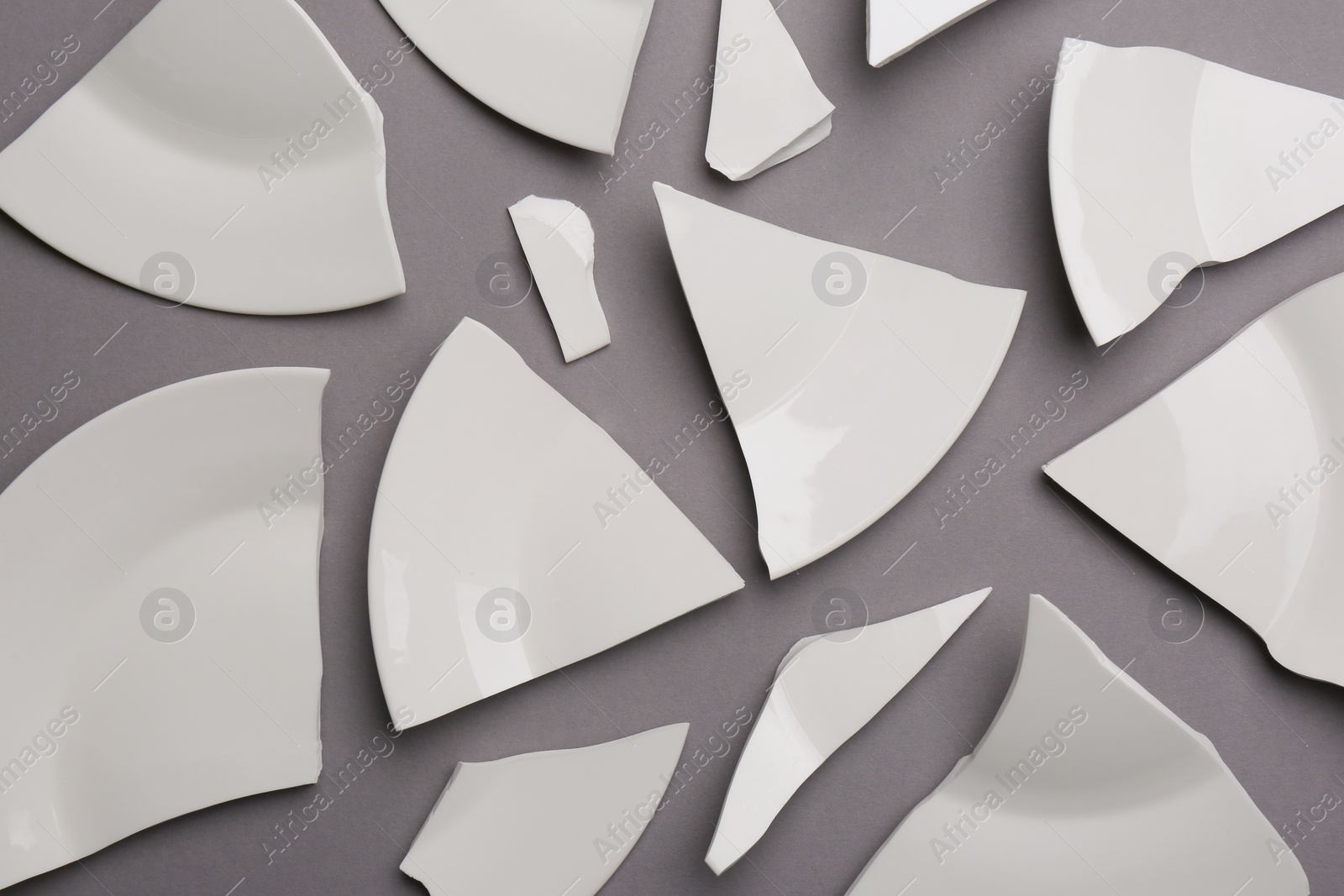 Photo of Pieces of broken white ceramic plate on grey background, flat lay