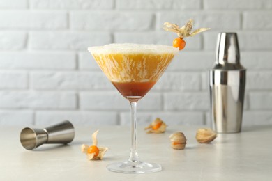 Photo of Delicious cocktail decorated with physalis fruit on light table near white brick wall