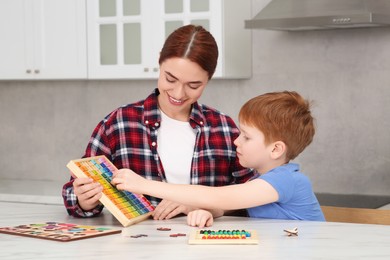 Photo of Happy mother and son playing with different colorful cubes and equations at white marble table in kitchen. Learning mathematics with fun