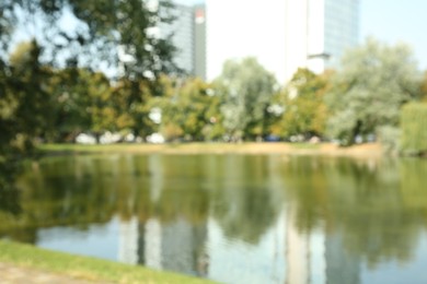 Blurred view of quiet park with trees and lake on sunny day