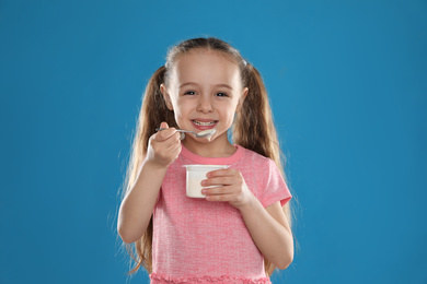Cute little girl eating tasty yogurt on blue background