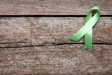 World Mental Health Day. Green ribbon on wooden background, top view with space for text