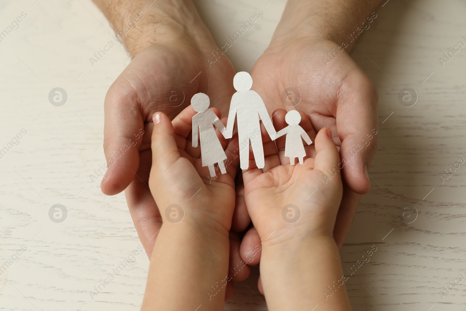 Photo of Father and child holding paper cutout of family at white wooden table, top view