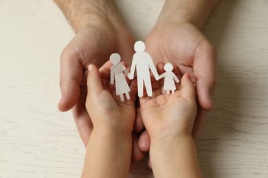 Father and child holding paper cutout of family at white wooden table, top view