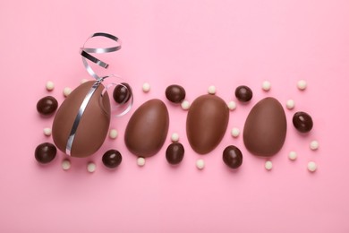 Delicious chocolate eggs and sweets on pink background, flat lay