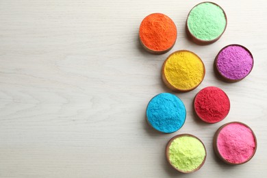 Colorful powder dyes on white wooden background, flat lay with space for text. Holi festival