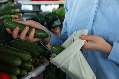 Photo of Woman putting cucumber into cotton eco bag at wholesale market, closeup. Life without plastic