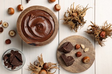 Photo of Bowl of tasty chocolate paste with hazelnuts on white wooden table, flat lay