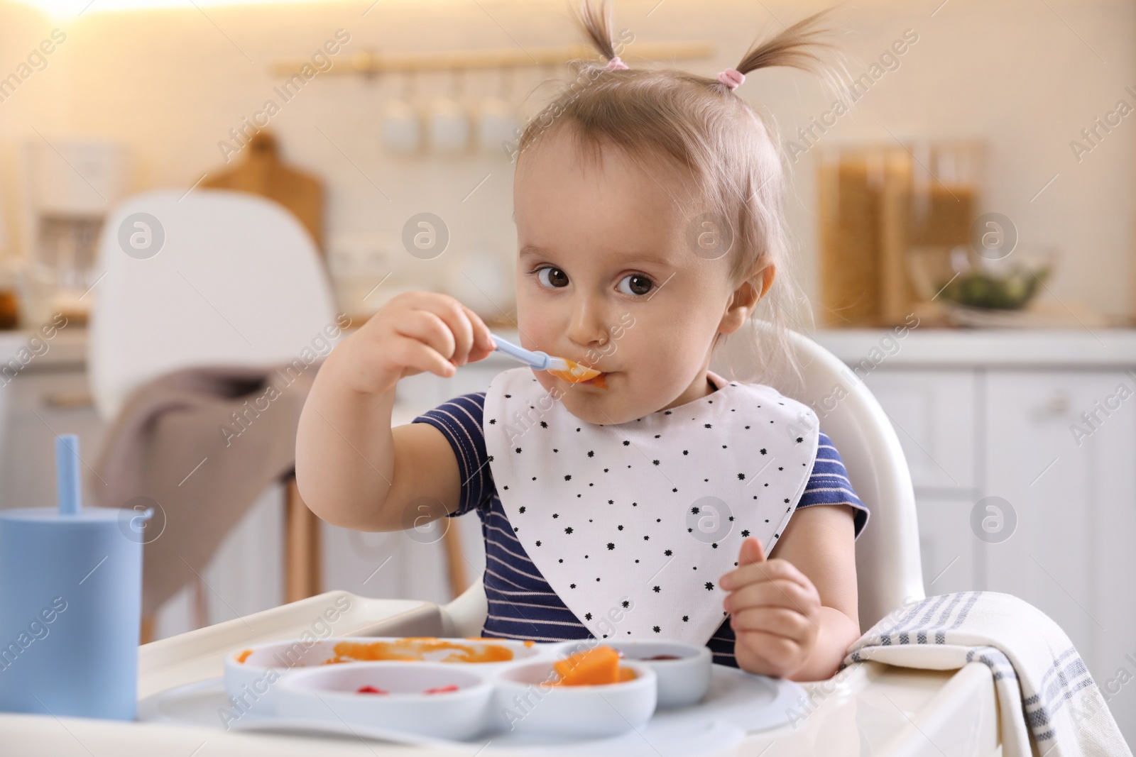 Photo of Cute little baby eating food in high chair at kitchen