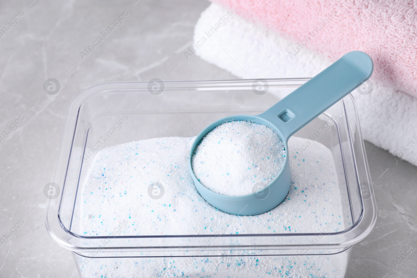 Photo of Container and measuring scoop with laundry powder on marble table