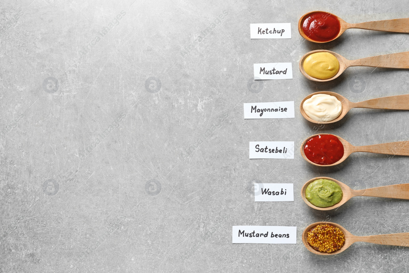 Photo of Different sauces in spoons and name tags on gray background, flat lay. Space for text