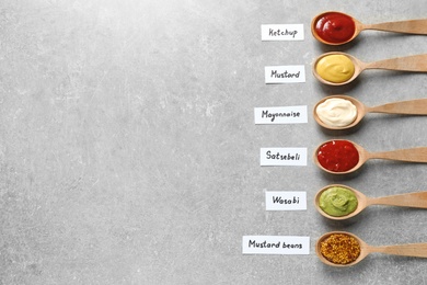 Photo of Different sauces in spoons and name tags on gray background, flat lay. Space for text