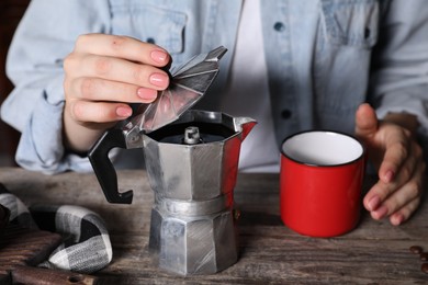 Brewing coffee. Woman with moka pot and cup at wooden table, closeup