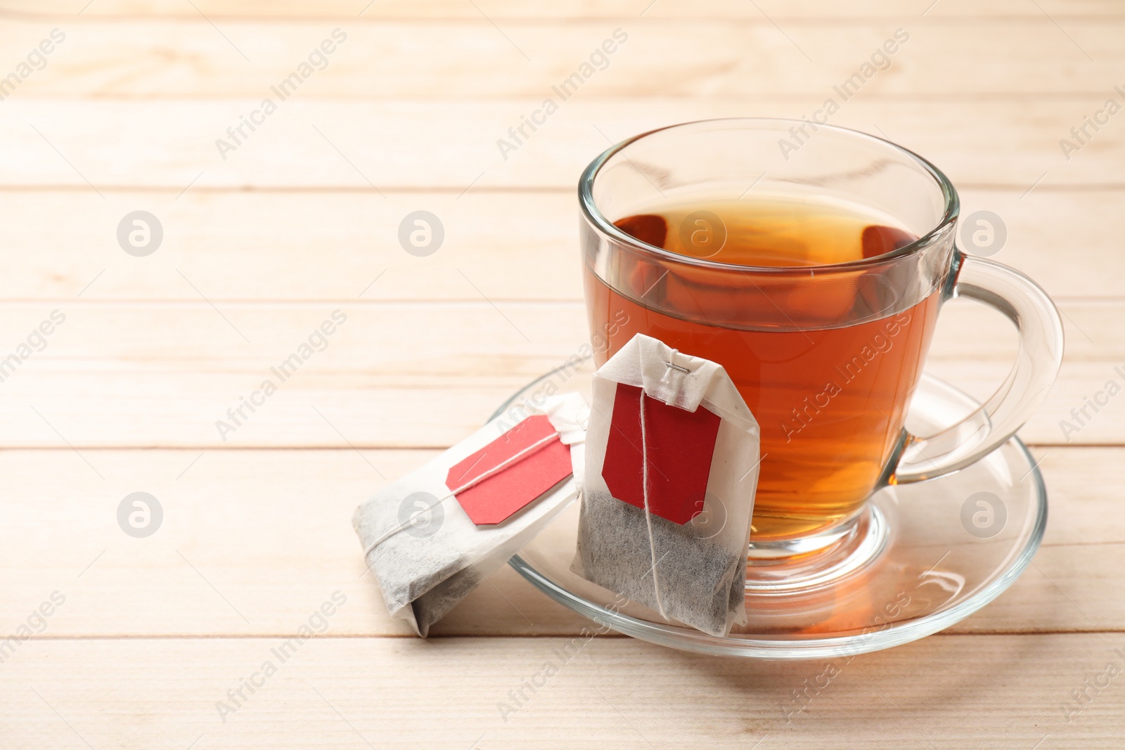 Photo of Tea bags and glass cup of hot beverage on light wooden table, space for text