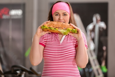 Overweight woman eating sandwich in gym