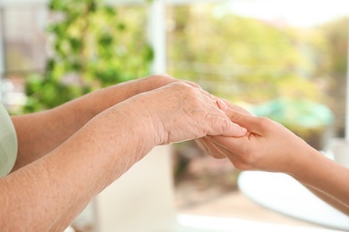 Photo of People holding hands together on blurred background, closeup. Help and elderly care concept