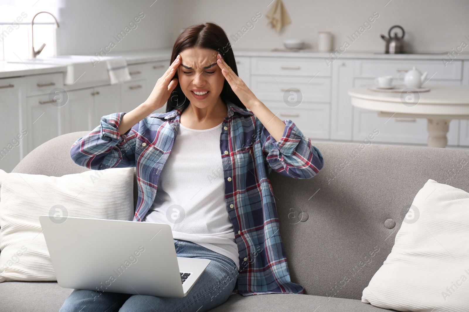 Photo of Young woman with laptop suffering from migraine at home